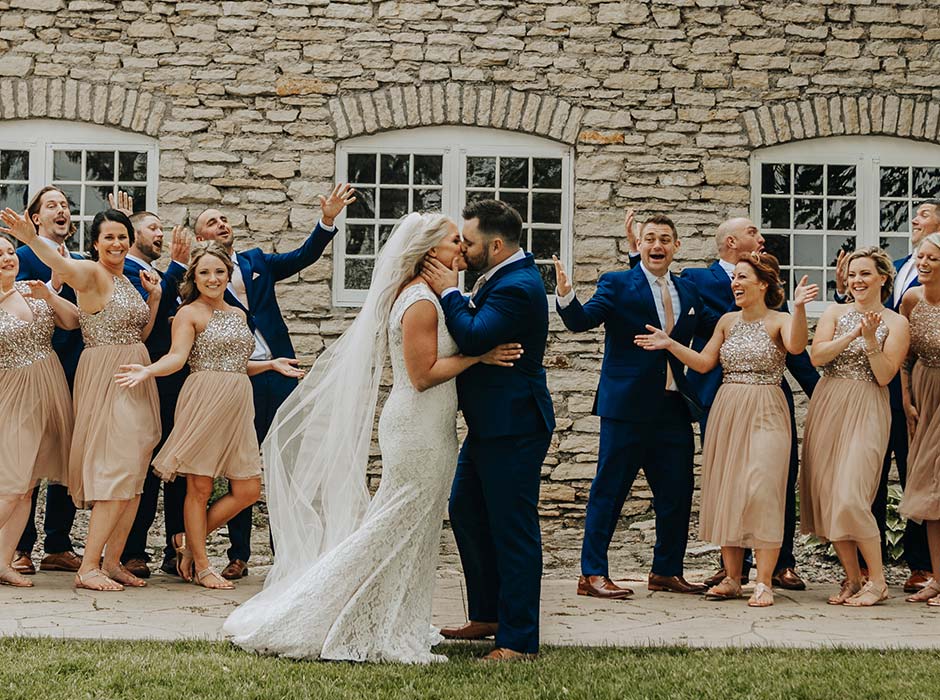 Bride and Groom along with wedding party share kiss outside the Mayowood Stone Barn wedding and event venue in Rochester MN