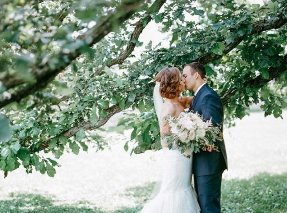 Bride and Groom share first kiss at Mayowood Stone Barn wedding venue in Rochester MN under the old oak tree