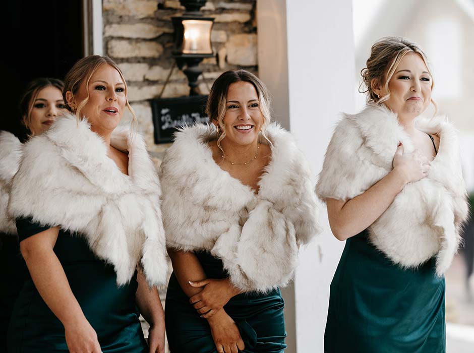 Bridesmaids in fur coats and green dresses at Mayowood Stone Barn the best winter wedding barn and event venue in Rochester MN